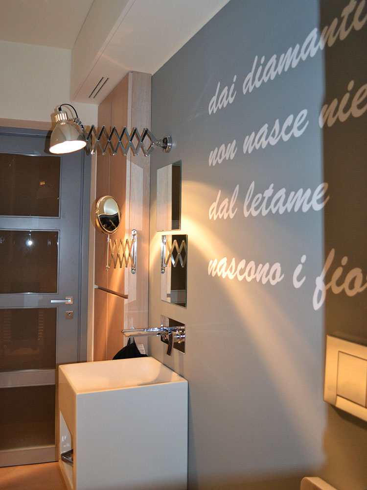 Bagno dello studio con citazione di Fabrizio De André tratta da “Via del Campo”, lavabo geometrico e specchi modulari.