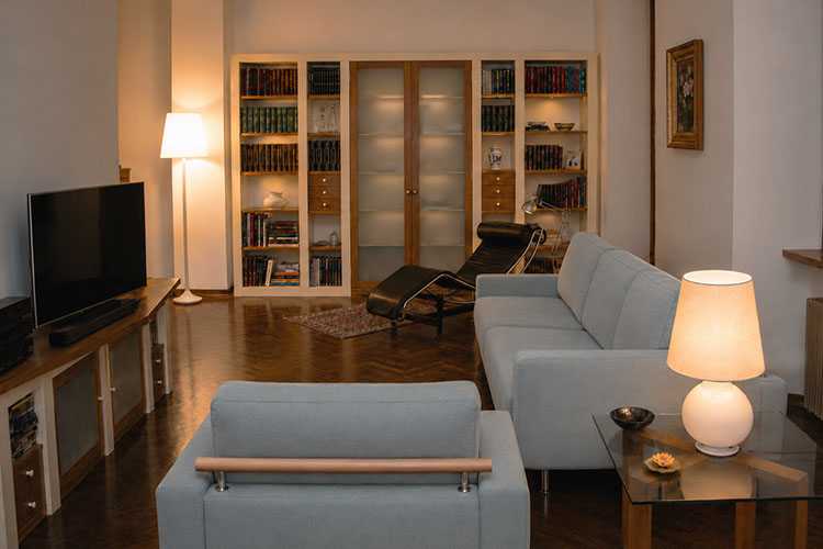 Soggiorno di un appartamento storico con libreria su misura, divani azzurro acqua e soffitto decorato.